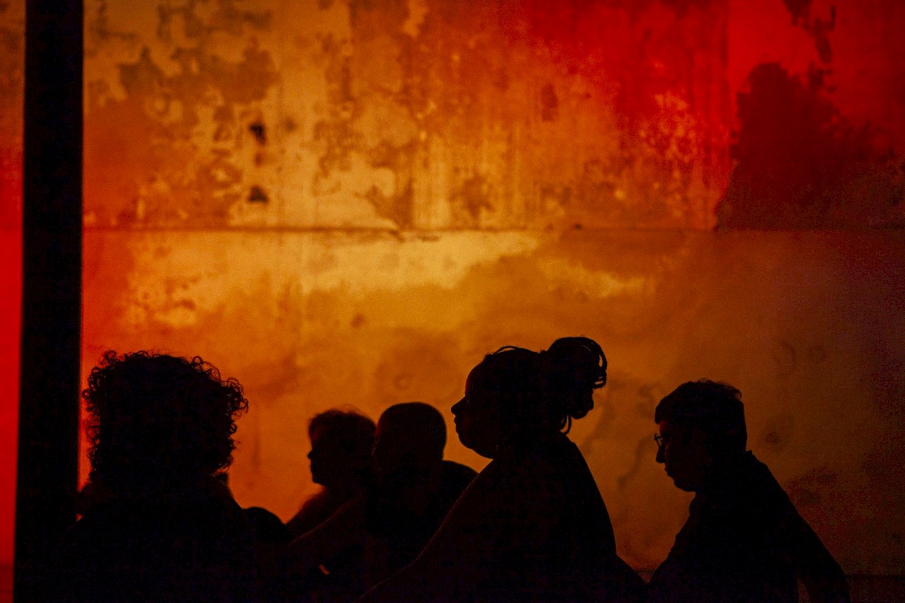 ALKANARA - Silhuetas de pessoas num cenário quente, iluminado a vermelho e amarelo. - ©Aline Belfort