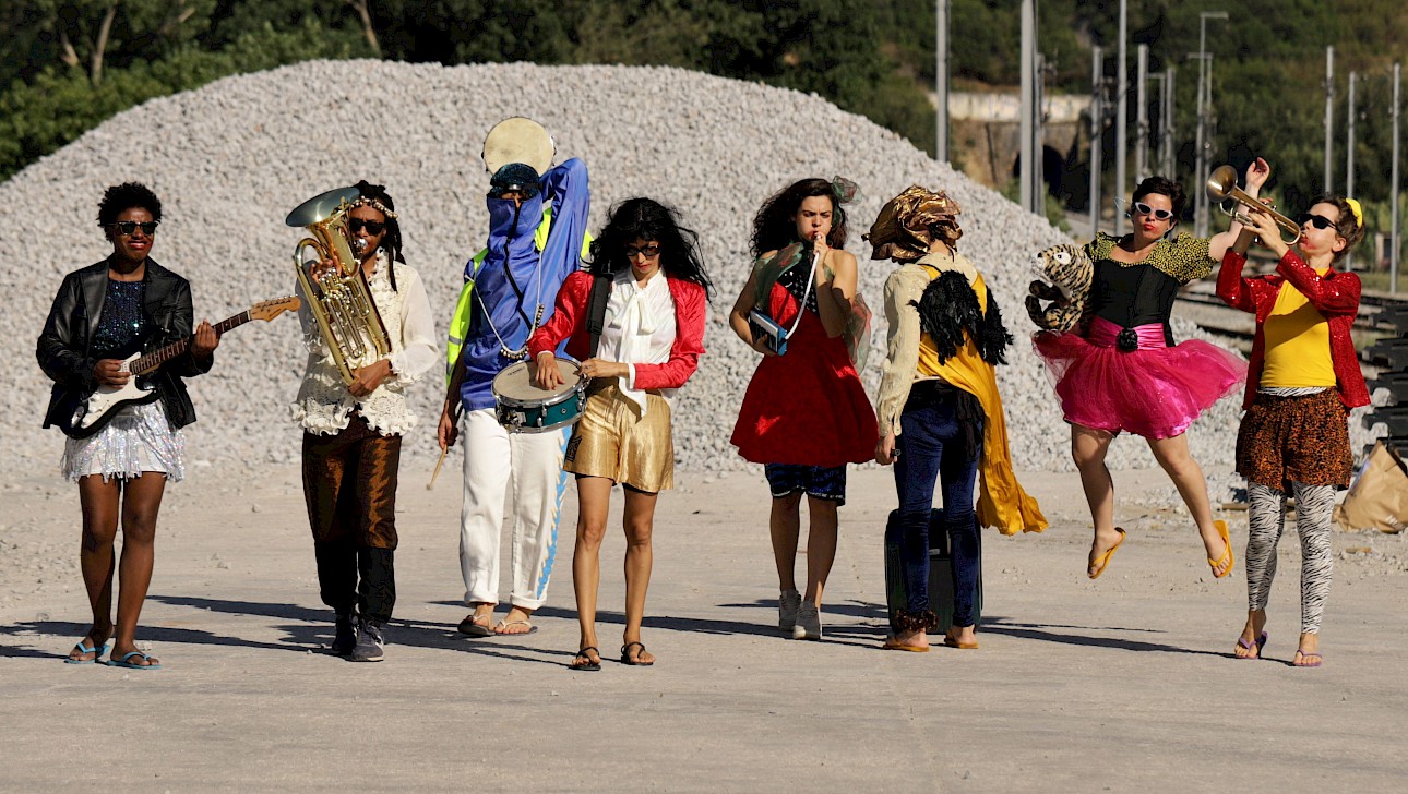 ALKANARA - A diverse group of people in colorful costumes, joyfully holding various musical instruments together. - ©Walesca Timmen