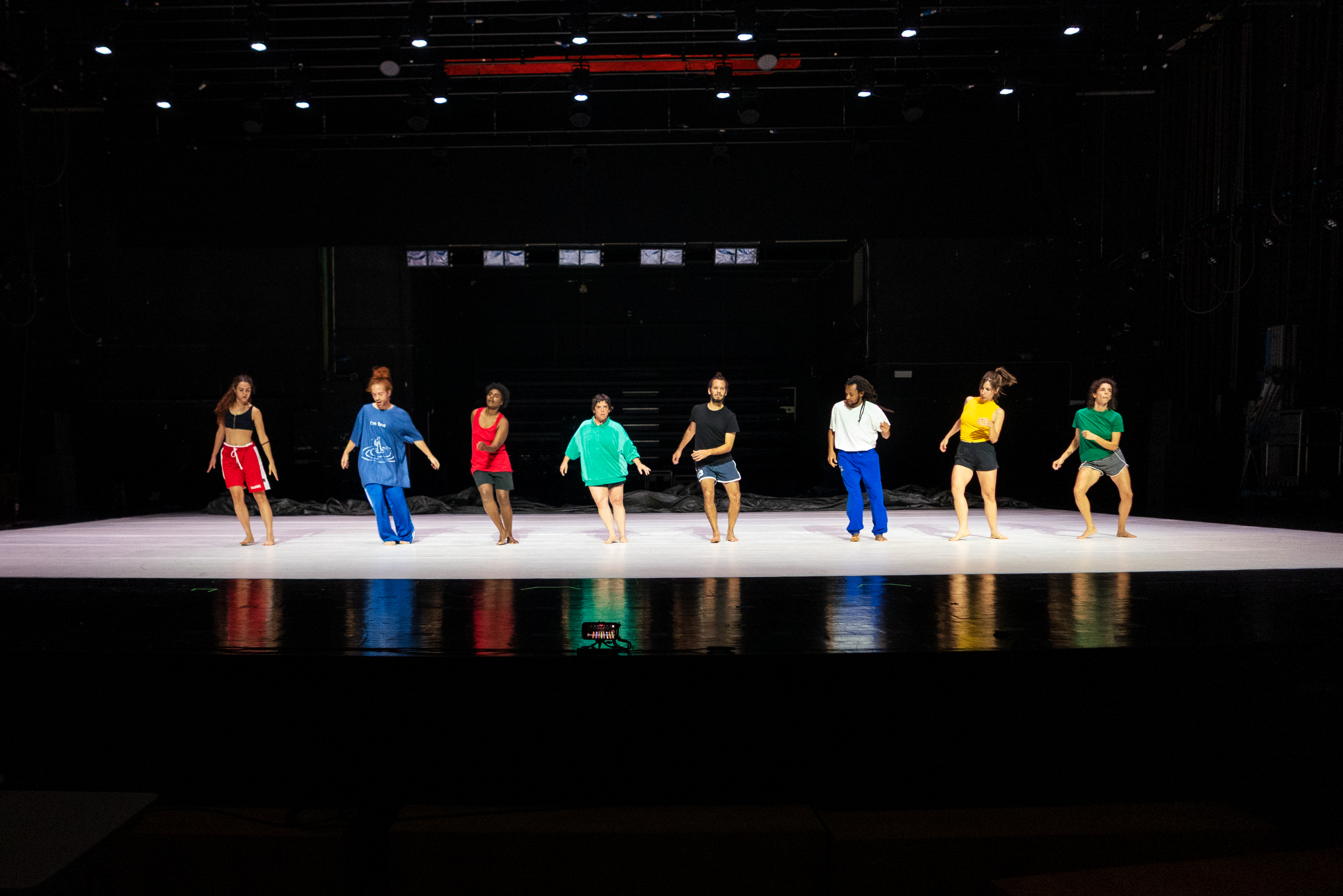 A group of eight dancers performs on stage, wearing colorful outfits. - Walesca Timmen