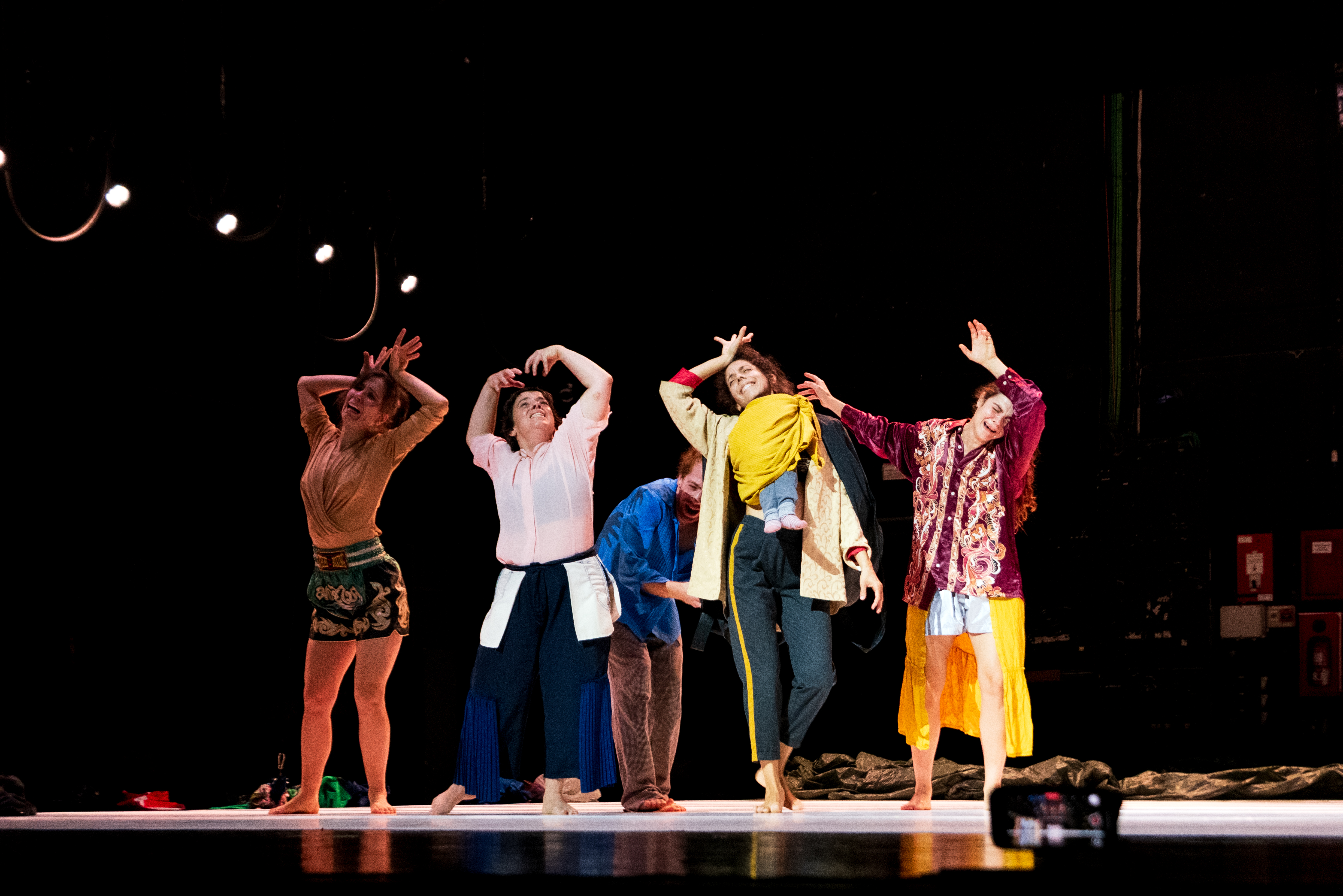 Five people perform on stage, each striking different expressive poses with raised arms and distinct outfits under stage lights. - Walesca Timmen